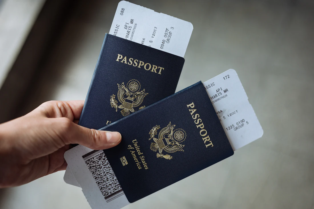 A hand holding two passports with paper boarding passes tucked inside