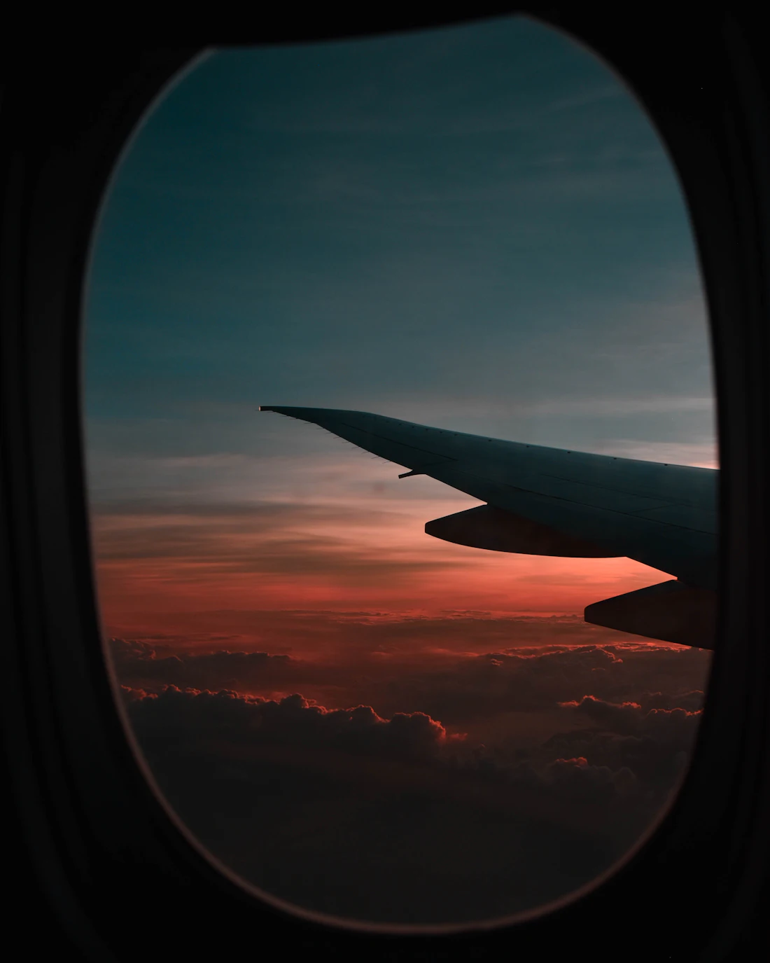 View through an aircraft window of a wing above clouds at sunset