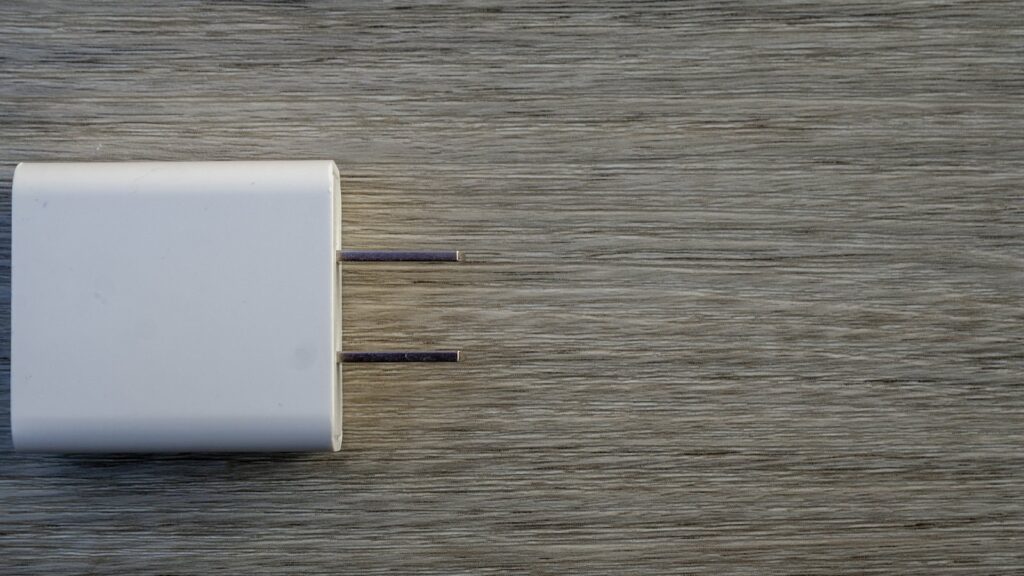 A white wall charger with two metal prongs lying on a grey wooden surface