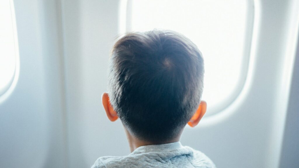A young child seen from behind, looking out of a bright aircraft window