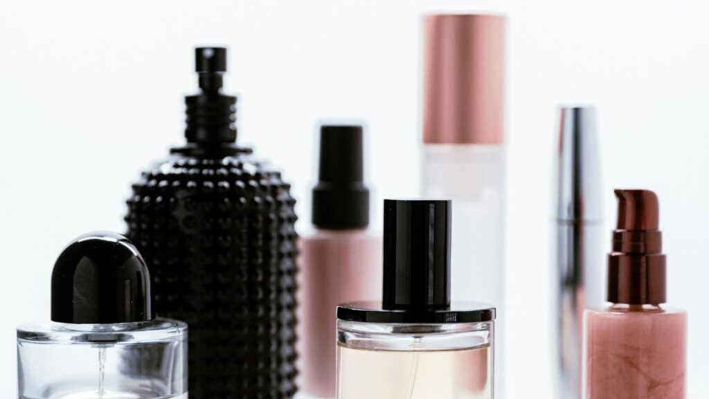 A row of glass perfume and cosmetic bottles with black and rose-gold caps against a white background