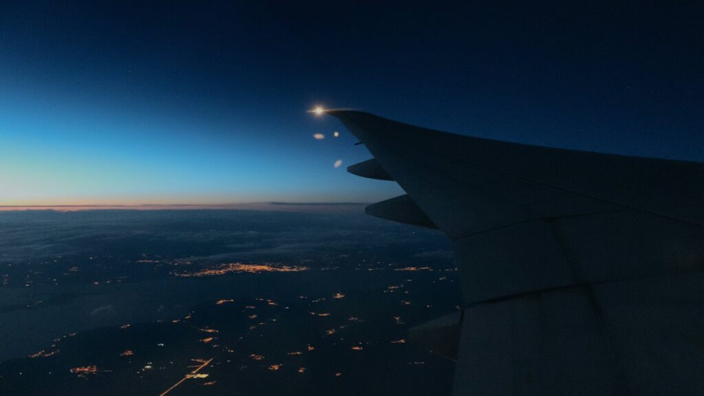 An aircraft wing against a deep blue night sky above the scattered lights of towns below